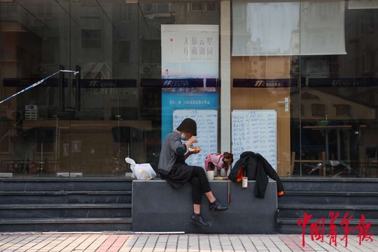  5月3日，上海市黄浦区，“电话亭女士”与她的狗“丽丽”正在一家暂停营业的房屋中介门前吃午饭。中青报·中青网记者 李强/摄